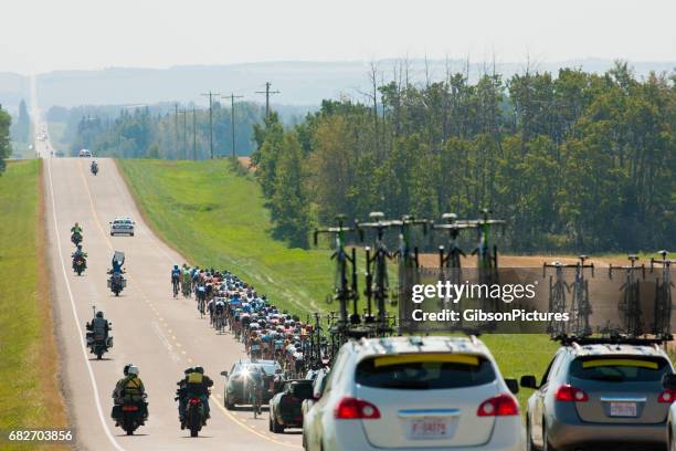 a large group of male bicycle racers ride together in a peloton during a professional road bike race. - following car stock pictures, royalty-free photos & images