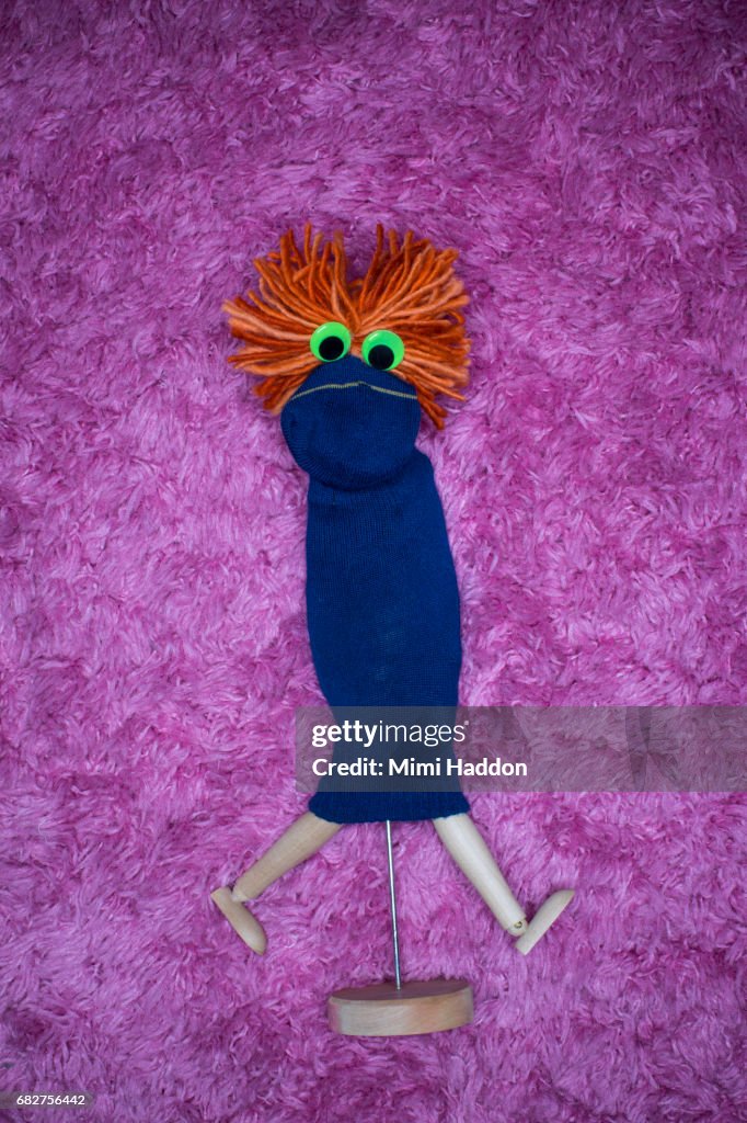 Blue Sock Puppet with Googly Eyes Walking on Pink Rug