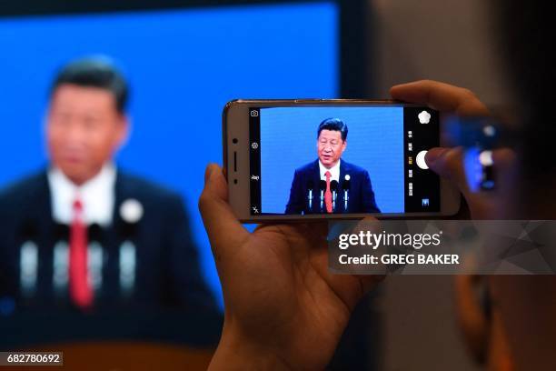 Journalist takes a photo of a live feed of China's President Xi Jinping speaking at the opening ceremony of the Belt and Road Forum, on a screen in...