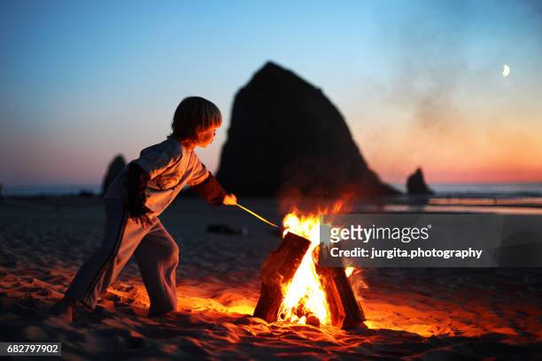 little boy by bonfire on the beach - kid stock stock-fotos und bilder