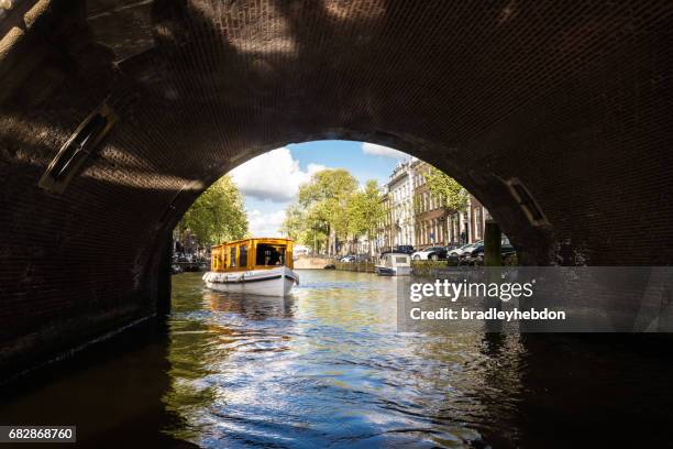 tourboat about to go under a bridge on amsterdam canal - amsterdam bridge stock pictures, royalty-free photos & images