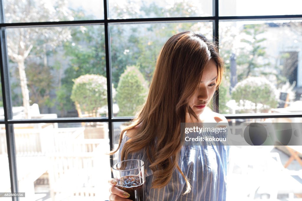 The woman stands by the window with coffee.