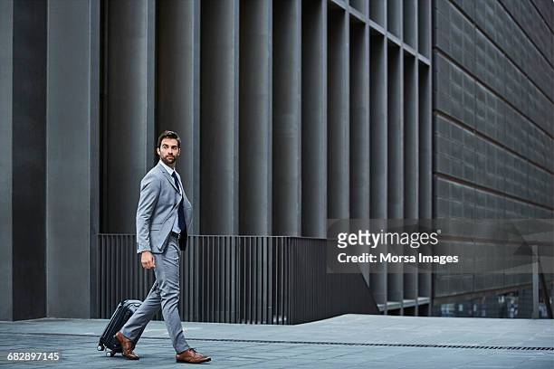 confident businessman with bag against building - pak stockfoto's en -beelden