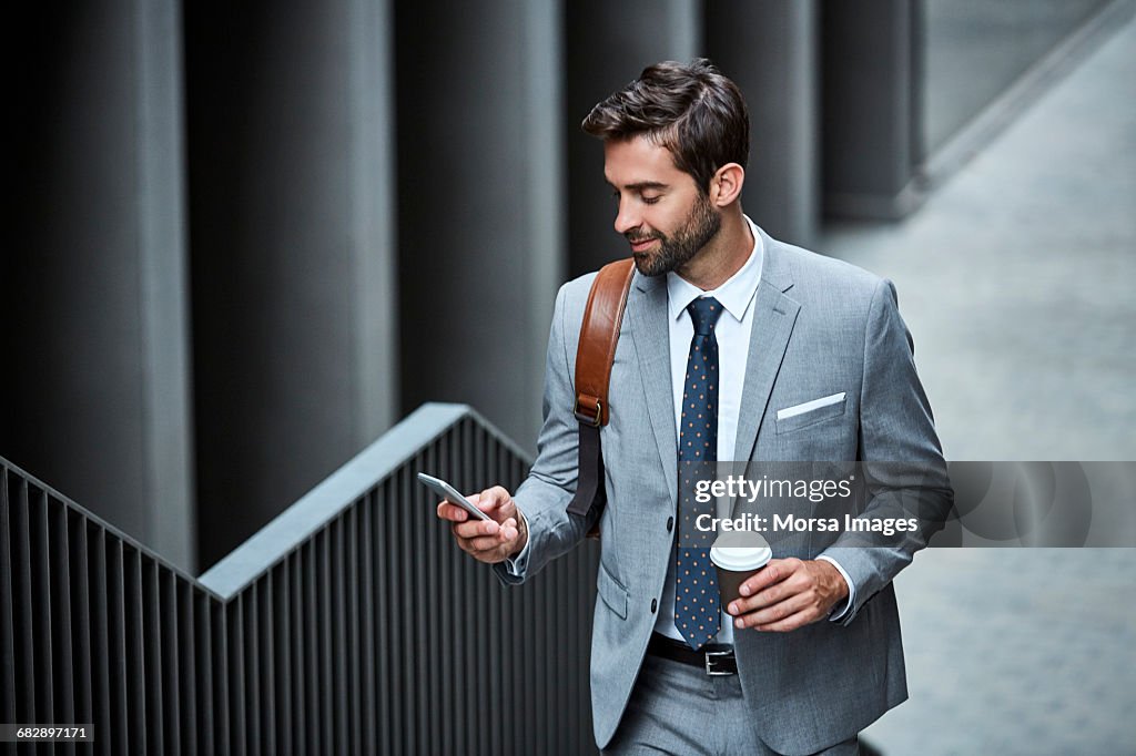 Businessman with cup and mobile phone on stairs