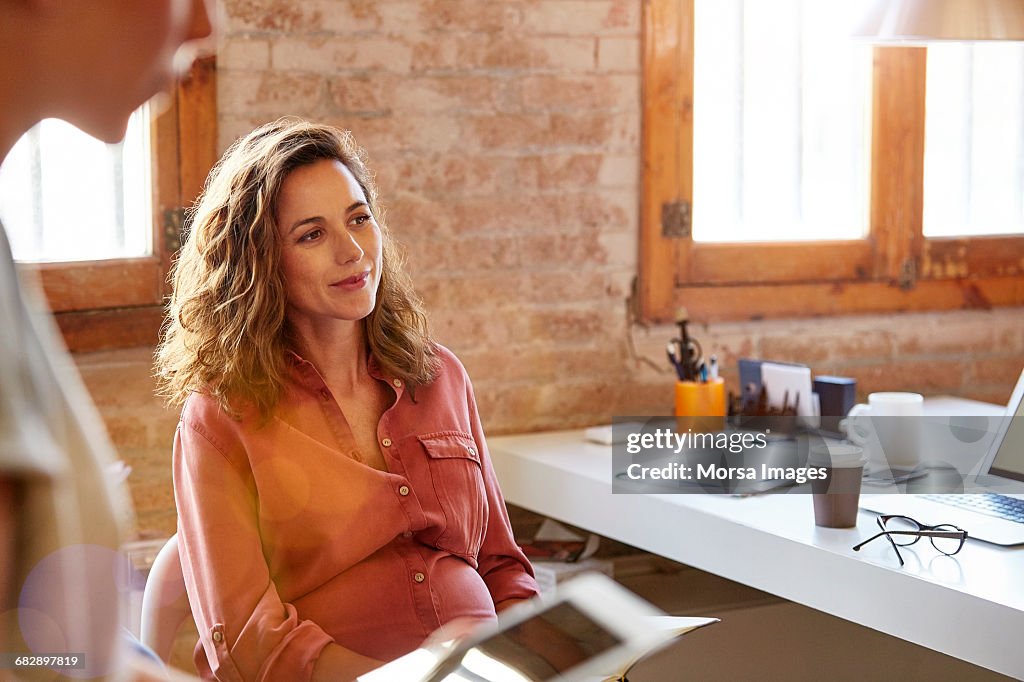 Pregnant businesswoman looking away at desk