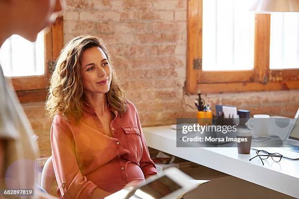 pregnant businesswoman looking away at desk - blusa cor de laranja imagens e fotografias de stock