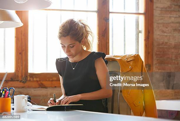 businesswoman writing in book at desk - schreibblock stock-fotos und bilder