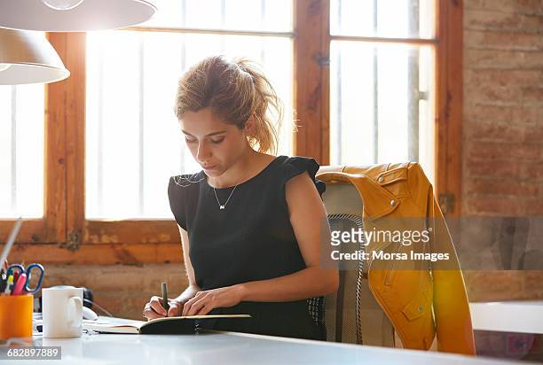 businesswoman writing in book at desk - sitting working stockfoto's en -beelden