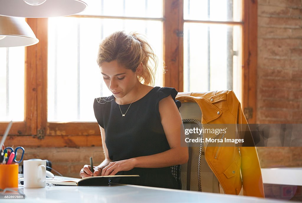 Businesswoman writing in book at desk