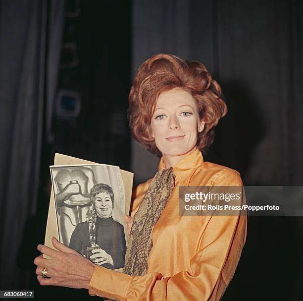 English actress Maggie Smith pictured holding a photograph of American actress Alice Ghostley accepting the Academy Award for Best Actress on behalf...