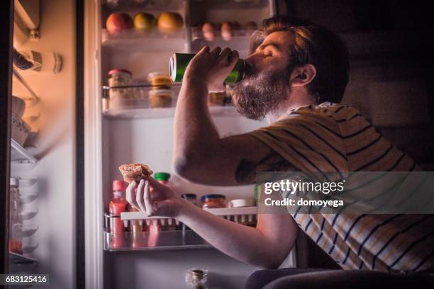 young bärtiger mann mit einem bier und late-night-snack vor dem kühlschrank - beer fridge stock-fotos und bilder