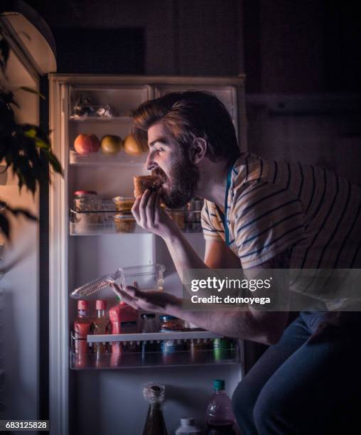 schönen jungen mann essen spät in die nacht vor dem kühlschrank - mitternacht stock-fotos und bilder