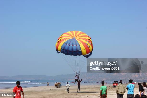 parachuter gliding over a populated beach - parasailing stock pictures, royalty-free photos & images