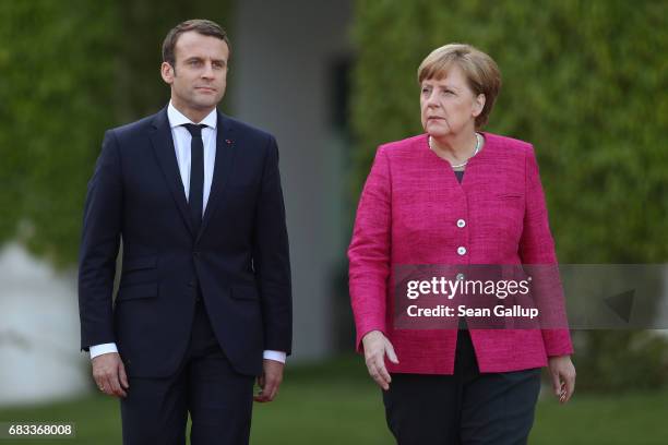 Newly-elected French President Emmanuel Macron and German Chancellor Angela Merkel walk to review a guard of honour upon Macron's arrival at the...