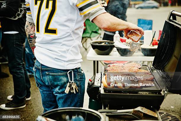 man seasoning burgers on grill at tailgating party - tailgate stock pictures, royalty-free photos & images