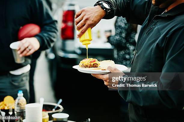 man putting mustard on burger at tailgating party - salsa de acompañamiento fotografías e imágenes de stock
