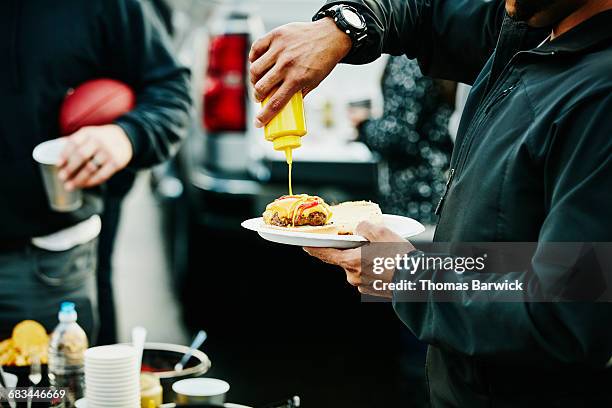 man putting mustard on burger at tailgating party - tailgating stock pictures, royalty-free photos & images