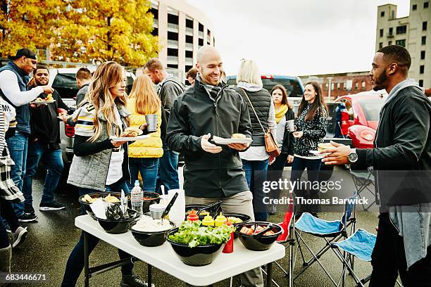 friends putting condiments on burgers during party - tailgating stock-fotos und bilder