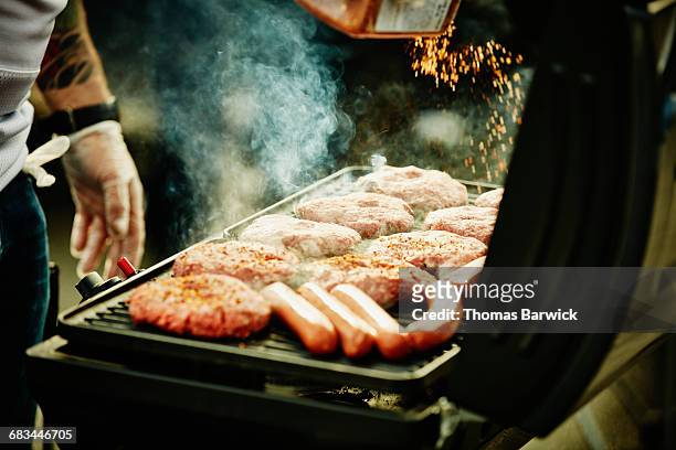 man seasoning burgers and hot dogs on barbecue - barbecue cibo foto e immagini stock