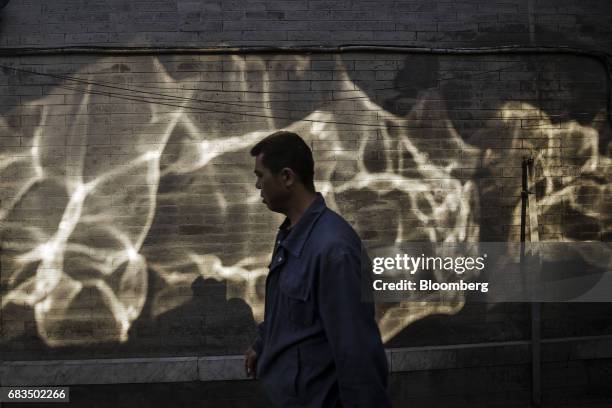 Pedestrian walks past reflections of light falling on a wall in a traditional hutong neighborhood in Beijing, China, on Sunday, May 14, 2017. Chinas...