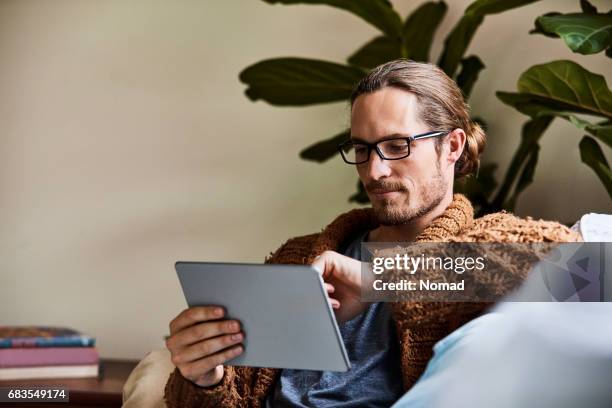 man using tablet computer while sitting on sofa - pullover stock pictures, royalty-free photos & images