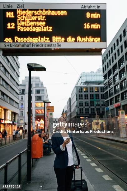 businesswoman waiting to use public transport  in the city - departure board front on fotografías e imágenes de stock
