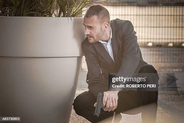 man in business attire behind plant pot holding handgun - mob ストックフォトと画像