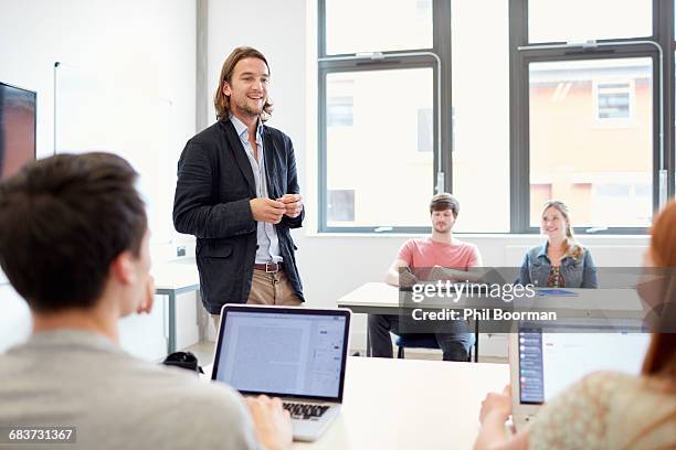 male lecturer teaching students using laptops in higher education college classroom - computer demonstration stock pictures, royalty-free photos & images