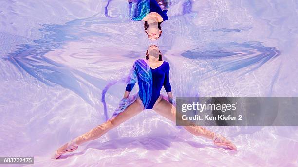 underwater view of girl wearing blue leotard and ballet shoes, facing surface of water - body foto e immagini stock