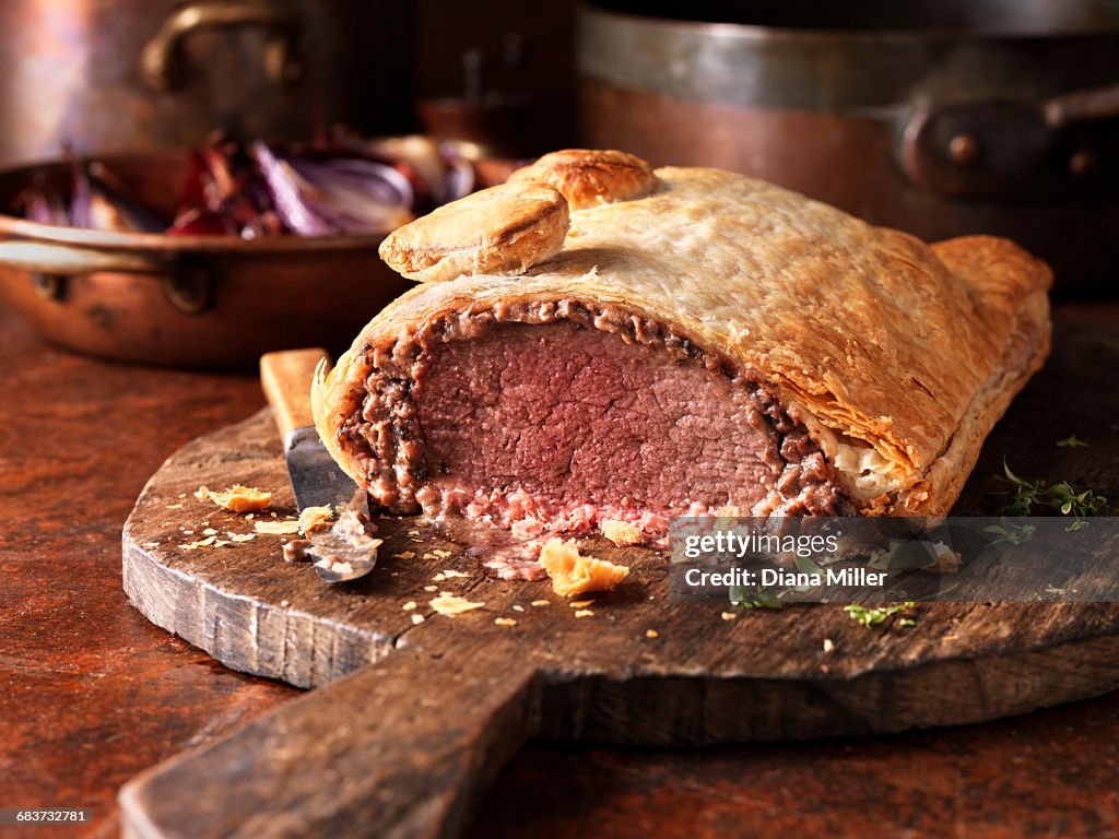 Roast beef wellington, red onions in background, fresh thyme