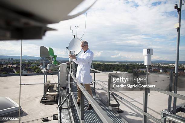 male meteorologist updating meteorological equipment measurements at rooftop weather station - meteorologe stock-fotos und bilder