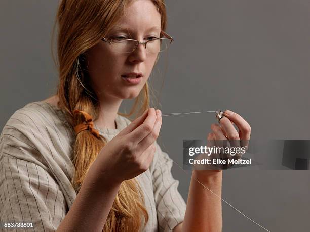 young female designer threading a sewing needle - mani fili foto e immagini stock