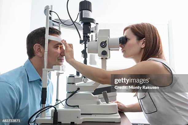 optician looking into patients eyes at small business opticians - eye exam stock pictures, royalty-free photos & images