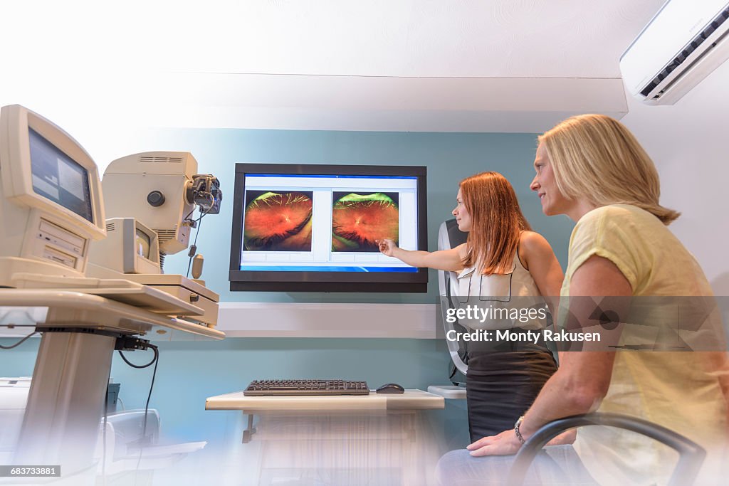 Optician discussing images of inside of patients eyes at small business opticians