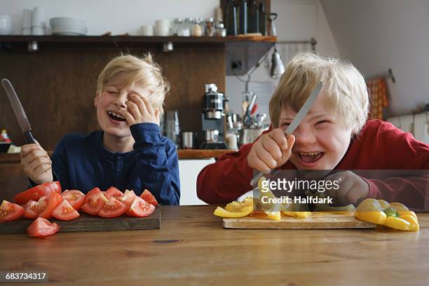 happy brothers holding knives at table with vegetables in kitchen - gele paprika stockfoto's en -beelden