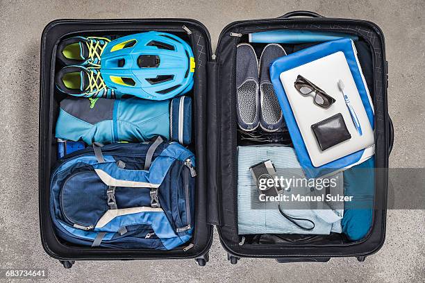 overhead view of open packed suitcase with blue shirt, bike helmet, backpack, retro camera and toothbrush - open backpack stock pictures, royalty-free photos & images