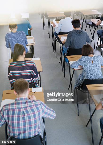 college students taking test at desks in classroom - tentamenzaal stockfoto's en -beelden