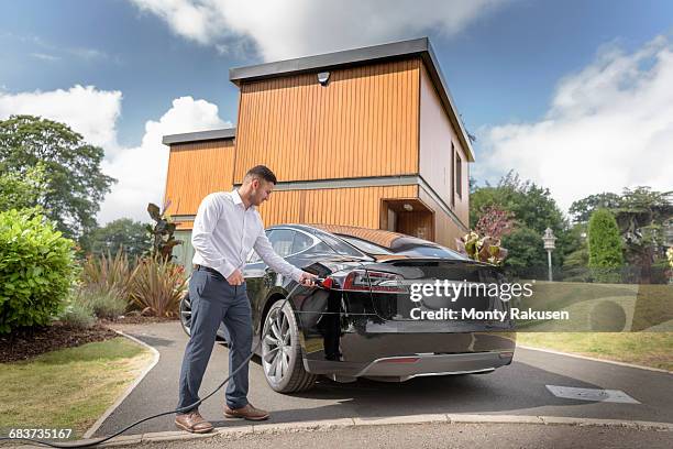 man charging electric car outside modern house - electric car home stock pictures, royalty-free photos & images