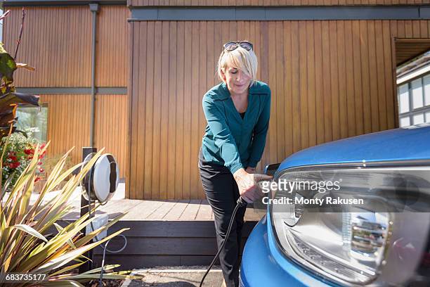 woman charging electric car from charging point - cargar fotografías e imágenes de stock