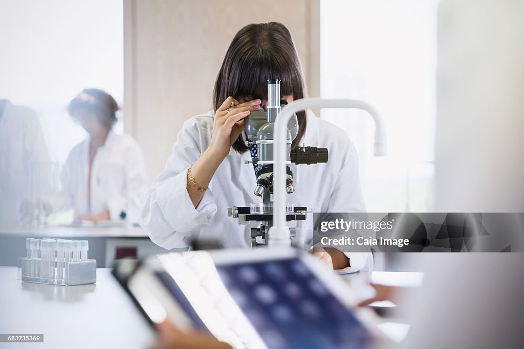 Female college student using microscope in science laboratory classroom
