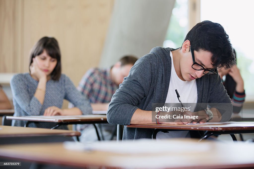 Focused male college student taking test at desk in classroom