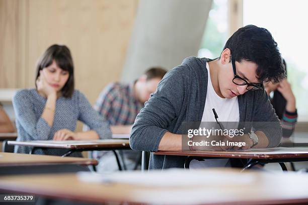 focused male college student taking test at desk in classroom - tentamenzaal stockfoto's en -beelden