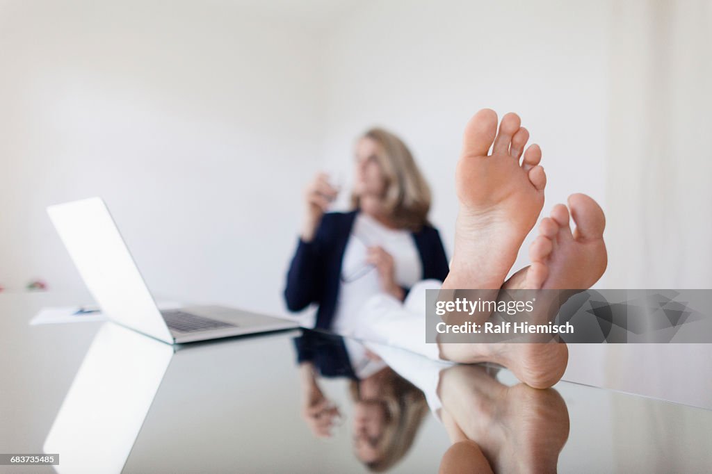 Woman with legs crossed at ankle resting by laptop on table in office