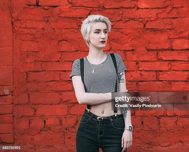 confident young woman standing against red brick wall - women in suspenders stock pictures, royalty-free photos & images