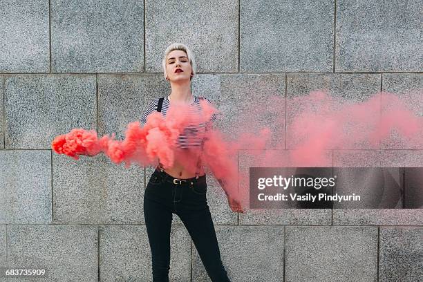 confident young woman standing with distress flare against wall - rebel stock-fotos und bilder