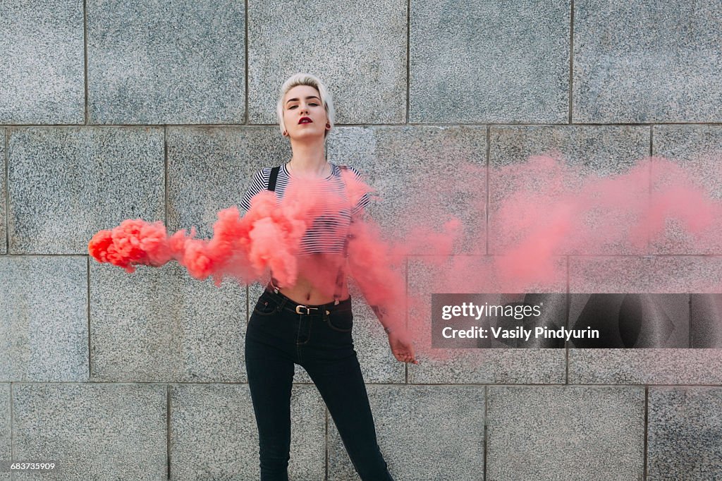 Confident young woman standing with distress flare against wall