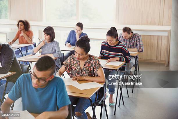 college students taking test at desks in classroom - tentamenzaal stockfoto's en -beelden