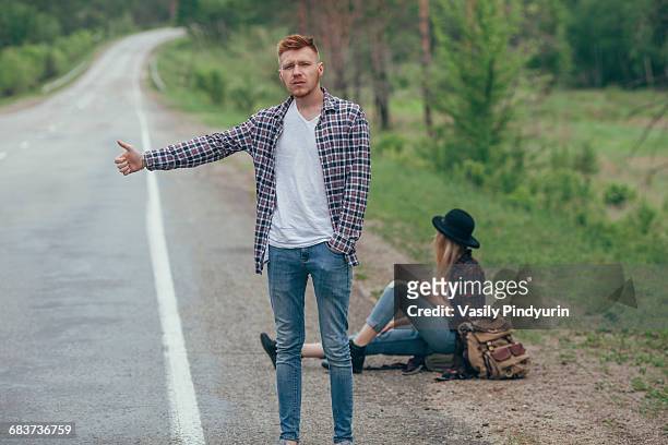 man hitchhiking while woman sitting on roadside - hitchhiking 個照片及圖片檔