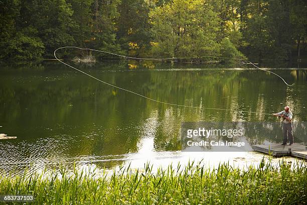 senior man fly fishing on green summer lake - fishing line stock pictures, royalty-free photos & images