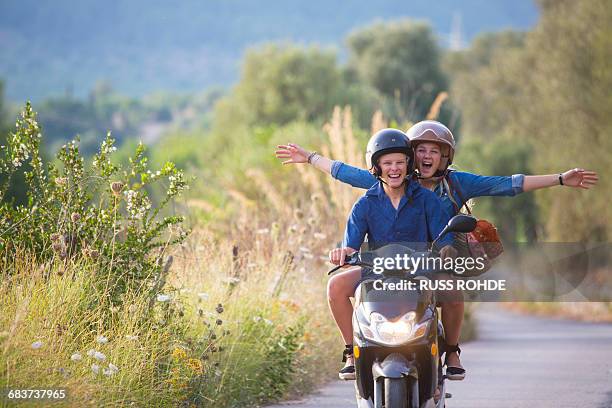 young woman riding pillion on moped with arms open on rural road, majorca, spain - holiday scooter fotografías e imágenes de stock